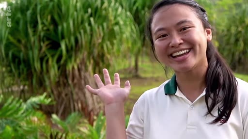 Une jeune femme souriante fait un signe de la main devant la caméra dans un paysage verdoyant, illustrant le thème de la plantation d'arbres et de la nature.