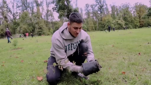 Un jeune homme portant un sweat-shirt Oregon est agenouillé dans un champ pour planter un jeune arbre, illustrant les initiatives de reforestation et de plantation d'arbres.