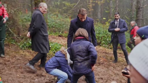 Le président français Emmanuel Macron participe à une opération de reforestation en forêt, entouré de collaborateurs et de participants. Cette séquence illustre l'engagement présidentiel en faveur de la préservation des écosystèmes forestiers en France.