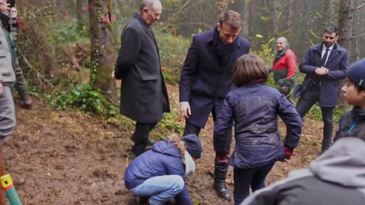 Le président français Emmanuel Macron participe à une opération de reforestation en extérieur, entouré de plusieurs personnes dont des enfants qui plantent des arbres dans la boue. Cette séquence illustre l'engagement présidentiel en faveur de la protection de l'environnement et de la gestion forestière.