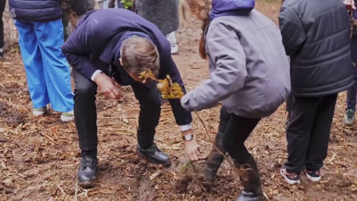 Le président français Emmanuel Macron participe à une opération de plantation d'arbres en extérieur, accompagné d'enfants. Cette séquence illustre les initiatives de reforestation et l'engagement environnemental du chef de l'État.