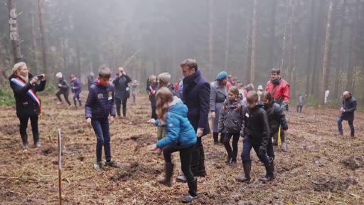 Le président français Emmanuel Macron est entouré d'enfants lors d'une activité de plantation d'arbres dans une forêt brumeuse, illustrant les initiatives de reforestation en France.