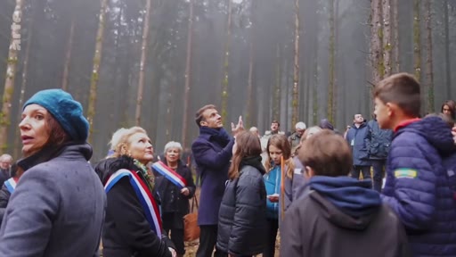 Le président français Emmanuel Macron, accompagné d'élus locaux portant l'écharpe tricolore et d'un groupe d'enfants, observe la canopée lors d'une visite en forêt dans le cadre d'une initiative de plantation d'arbres.