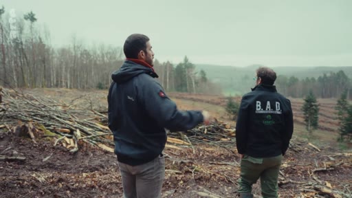 Deux hommes, dont l'un porte une veste marquée B.A.D., inspectent une zone de déforestation et de coupe rase en forêt lors d'un reportage sur les pratiques sylvicoles.