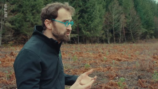 Un homme barbu avec des lunettes bleues discute en extérieur dans une zone de forêt, illustrant le sujet de l'opposition sociale à la sylviculture industrielle.