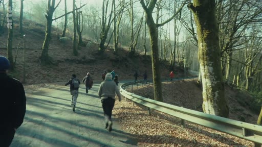 Un groupe de personnes, potentiellement des manifestants, court sur une route goudronnée bordée d'arbres au Bois du Chat. La scène illustre une situation de tension ou de mouvement rapide dans un contexte de manifestation ou d'affrontement.