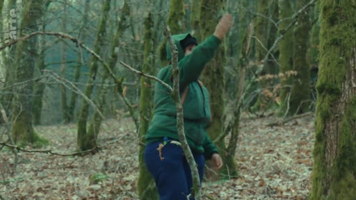 Une personne portant une veste verte à capuche évolue dans la zone boisée du Bois du Chat, dans le cadre des manifestations et des tensions sur place.