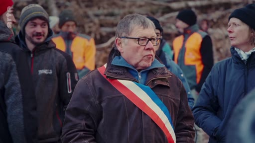 Un maire portant l'écharpe tricolore officielle s'exprime lors d'un rassemblement de professionnels de la filière bois en forêt. Il est entouré de plusieurs personnes, dont certaines portent des gilets de sécurité orange, dans un contexte de mobilisation ou de visite de terrain.