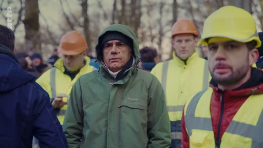 Des travailleurs forestiers portant des casques de chantier et des gilets haute visibilité sont réunis en extérieur lors d'un rassemblement professionnel. Le groupe, composé d'hommes en tenue de travail, semble écouter attentivement dans un environnement boisé.