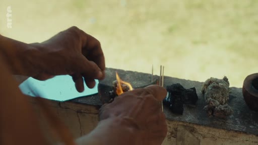 Gros plan sur les mains d'une personne Pataxó allumant des bâtons d'encens lors d'une cérémonie rituelle dans le territoire Pataxó au Brésil. Ce geste symbolique souligne les pratiques culturelles et spirituelles préservées par la communauté autochtone.