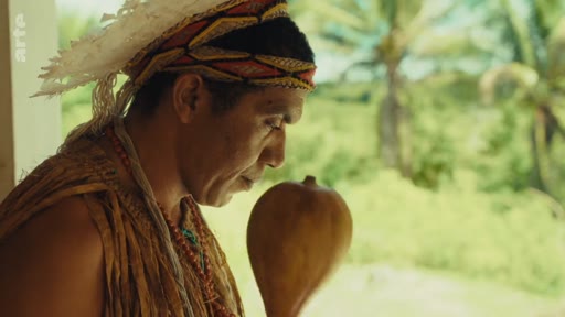 Un homme autochtone Pataxó, portant une coiffe traditionnelle et des ornements, tient une calebasse lors d'un rituel dans le territoire Pataxó au Brésil. Cette image illustre la préservation des traditions culturelles et l'identité des peuples autochtones face aux enjeux territoriaux.