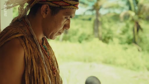 Un homme Pataxó portant une coiffe et des vêtements traditionnels est filmé de profil dans un environnement naturel, illustrant la culture et l'identité autochtone au Brésil.