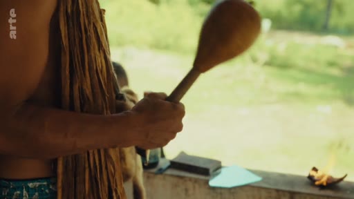 Un membre de la communauté autochtone Pataxó tient un instrument de musique traditionnel en bois lors d'une cérémonie ou d'un rassemblement dans le territoire Pataxó au Brésil. La scène illustre la préservation des traditions culturelles et l'identité des peuples autochtones.