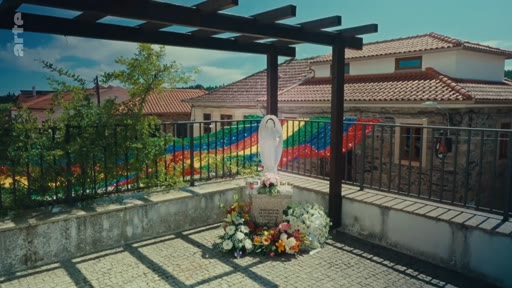Une statue de la Vierge Marie ornée de fleurs et une banderole aux couleurs vives installées en extérieur, en commémoration des incendies de forêt de 2017 au Portugal.