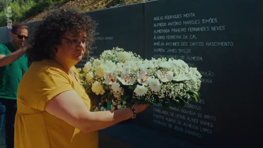 Une femme rend hommage aux victimes des incendies de 2017 au Portugal en déposant une gerbe de fleurs devant un monument commémoratif gravé des noms des disparus. La scène illustre le travail de mémoire et le recueillement des familles après la tragédie de Pedrógão Grande.