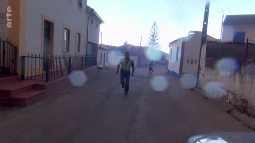Un homme court en direction de la caméra dans une rue résidentielle lors d'une évacuation liée à des incendies de forêt. La scène montre l'urgence et la désolation d'une zone évacuée.