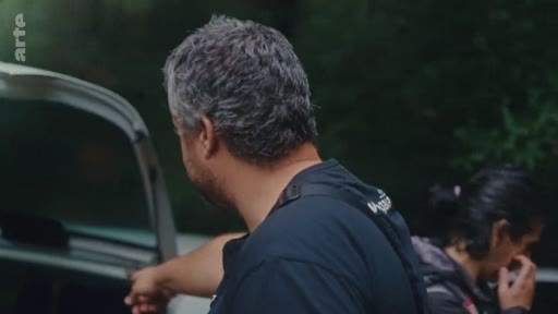 Un homme de dos et une femme en arrière-plan dans un environnement extérieur, dans le cadre d'un reportage sur l'éradication des eucalyptus.