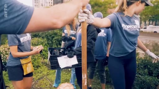 Un groupe de bénévoles portant des t-shirts uniformes participe à une opération de plantation d'arbres en ville, utilisant des outils de jardinage et des caisses de transport. Cette action s'inscrit dans le cadre d'initiatives citoyennes pour la végétalisation urbaine et la lutte contre le changement climatique.