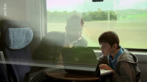 Un jeune garçon et un homme, probablement Felix Finkbeiner, travaillent sur un ordinateur portable à bord d'un train, illustrant les activités de l'organisation Plant for the Planet.