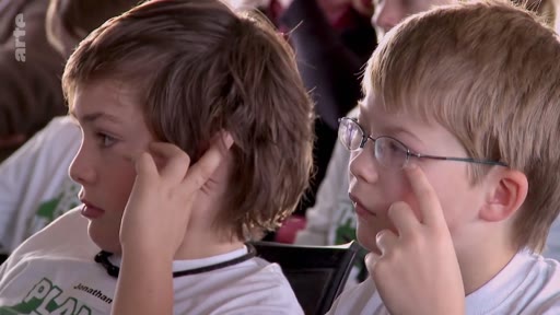 Deux jeunes garçons, dont l'un porte des lunettes, participent à un événement de l'organisation Plant-for-the-Planet. Ils portent des t-shirts blancs avec le logo de l'association et semblent attentifs lors d'une conférence ou d'un atelier.