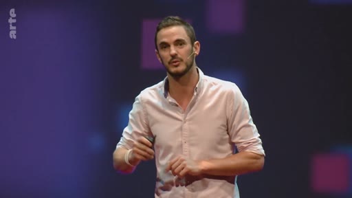Un présentateur masculin s'exprime sur scène lors d'une conférence, potentiellement liée à la crise climatique, devant un fond sombre avec des motifs géométriques.