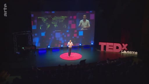 Un intervenant s'exprime sur scène lors d'une conférence TEDx Lausanne, illustrant son propos avec une carte mondiale de la reforestation projetée sur un écran géant en arrière-plan.