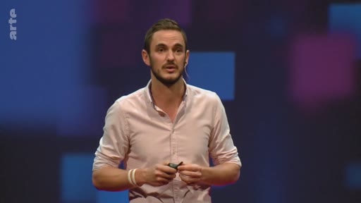 Un homme en chemise rose s'exprime sur scène devant un fond abstrait lors d'une conférence sur la reforestation mondiale.