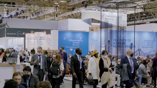 Des visiteurs et professionnels déambulent dans les allées d'un salon international, probablement la COP26, devant des stands consacrés aux perspectives nordiques et au développement durable. On peut lire des inscriptions sur les panneaux comme 'Choosing Green Nordic Perspectives' et 'The Path to a Green Nordic Region'.