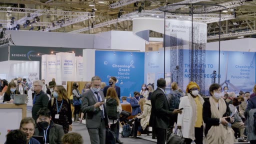 Vue d'ensemble du pavillon 'Choosing Green - Nordic Perspectives' lors d'un sommet international sur le climat, avec de nombreux délégués portant des masques sanitaires. Le stand met en avant le thème 'The Path to a Green Nordic Region' avec des visuels d'éoliennes.