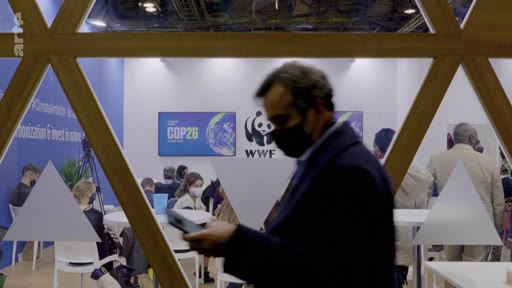 Un homme portant un masque circule devant le stand du WWF lors de la conférence sur le climat COP26. En arrière-plan, des participants sont assis à des tables dans l'espace d'exposition dédié aux enjeux environnementaux.