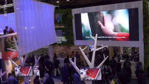 Vue d'ensemble d'un stand d'exposition lors d'un salon professionnel, mettant en avant un écran géant diffusant une vidéo montrant une main touchant un tronc d'arbre, illustrant des thématiques environnementales ou de développement durable.