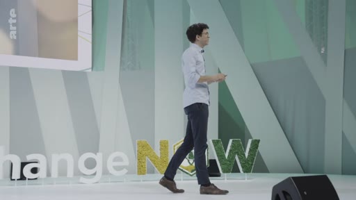Un intervenant masculin marche sur la scène de l'événement ChangeNOW, devant un décor végétalisé portant le logo de la conférence.