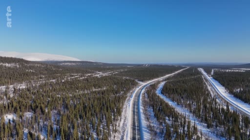 Vue aérienne d'une route asphaltée serpentant à travers une vaste forêt de conifères enneigée dans une région nordique, illustrant les paysages de la taïga.