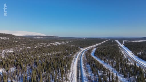 Vue aérienne d'une route asphaltée serpentant à travers une vaste forêt de conifères enneigée dans une région nordique, illustrant les paysages de taïga et les infrastructures de transport en milieu sauvage.
