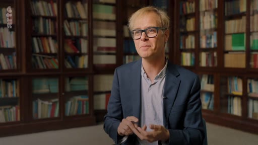 Un expert intervient dans une émission sur le rôle des écosystèmes de savane dans le cycle du carbone, filmé en plan moyen devant une bibliothèque.