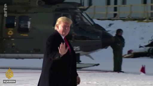 Donald Trump fait un signe de la main devant un hélicoptère militaire sur un terrain enneigé, lors d'un déplacement officiel.