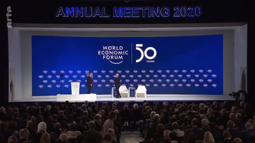 Vue d'ensemble de la scène lors de l'assemblée annuelle du Forum économique mondial 2020 à Davos, marquant le 50e anniversaire de l'organisation. Deux personnes sont présentes sur scène devant un écran géant affichant le logo du World Economic Forum.