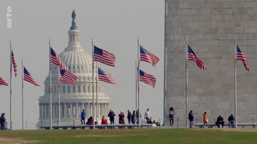 Vue panoramique du Capitole des États-Unis et du Washington Monument à Washington D.C., avec des drapeaux américains flottant au premier plan et des visiteurs se promenant sur la pelouse.