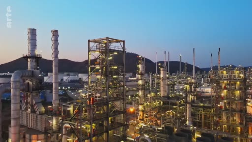 Vue aérienne d'une vaste raffinerie de pétrole et d'installations industrielles pétrochimiques au crépuscule, illustrant les enjeux de la production d'énergie fossile et de la transition écologique.