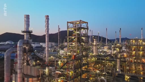 Vue aérienne d'une vaste raffinerie pétrolière avec ses tours de distillation et ses installations industrielles au crépuscule, illustrant les enjeux de la production d'énergie et de la compensation carbone.