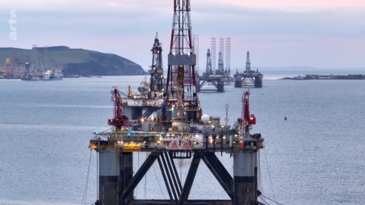 Vue d'ensemble d'une plateforme pétrolière offshore en activité, entourée d'autres structures industrielles dans une baie. Cette image illustre les infrastructures d'extraction d'hydrocarbures en mer.