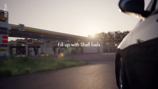 Une voiture roule vers une station-service Shell lors d'une campagne publicitaire mettant en avant les carburants de la marque. L'image illustre les stratégies de communication des entreprises pétrolières dans le cadre d'un reportage sur le greenwashing.
