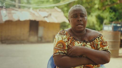 Une femme s'exprime face caméra lors d'un entretien en extérieur, évoquant probablement la lutte pour les terres ancestrales. Elle porte un vêtement traditionnel à motifs dans un cadre rural.