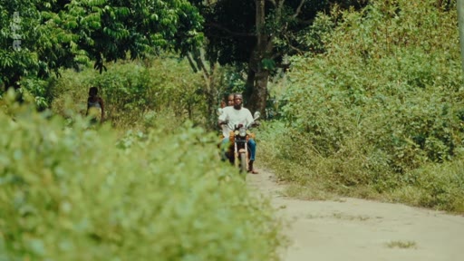 Deux personnes circulent à moto sur un chemin de terre dans une zone rurale, illustrant le contexte de la lutte pour les terres ancestrales.