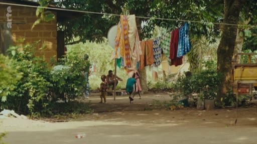 Des enfants jouent dans une cour de maison en zone rurale, avec du linge séchant sur une corde à linge, illustrant la vie quotidienne dans un village.