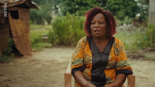 Une femme s'exprime face caméra lors d'une interview en extérieur, dans un cadre rural évoquant des conditions de vie précaires. Ce témoignage s'inscrit dans un reportage sur les difficultés économiques et la vie communautaire.