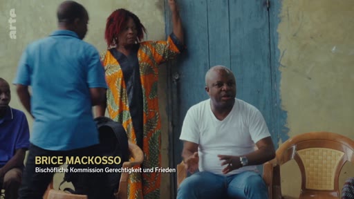Brice Mackosso, membre de la Bischöfliche Kommission Gerechtigkeit und Frieden, est interviewé dans un cadre informel. Il discute de questions liées à la justice et à la paix, probablement dans le contexte de conflits sociaux ou politiques.