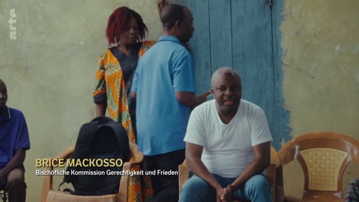 Brice Mackosso, membre de la Commission Justice et Paix, est interviewé dans un cadre informel. Il est identifié par un bandeau à l'écran, discutant probablement de questions de justice et de droits humains.