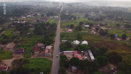 Vue aérienne plongeante sur une route rectiligne traversant un paysage rural avec des habitations dispersées, illustrant l'aménagement du territoire et l'urbanisation dans le cadre d'un reportage sur l'accaparement des terres.
