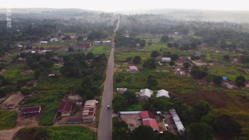 Vue aérienne plongeante sur une route goudronnée traversant un paysage rural avec des habitations éparses et une végétation dense, illustrant le développement territorial et l'aménagement du paysage dans le Sud global.